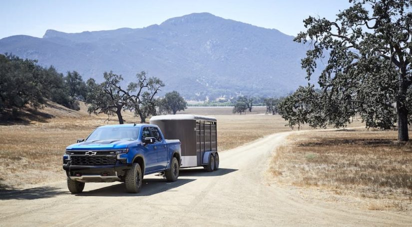 A blue 2022 Chevy Silverado 1500 ZR2 is shown towing a trailer on a dirt path.