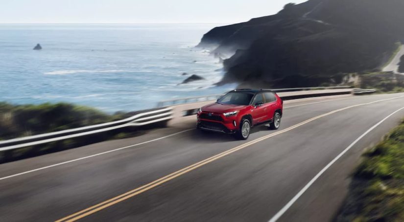 A red 2022 Toyota RAV4 Prime XSE is shown driving on a coastal road.
