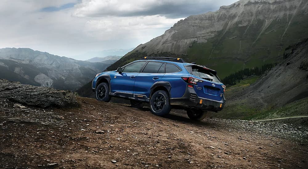 A blue 2022 Subaru Outback Wilderness is shown from the rear driving up a steep trail.