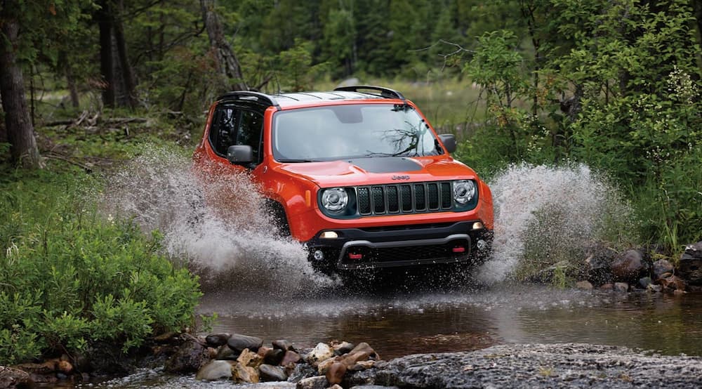 An orange 2020 Jeep Renegade is shown driving through a river.
