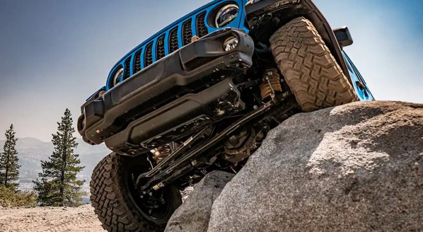 A blue 2022 Jeep Wrangler is shown off-roading on a rock.