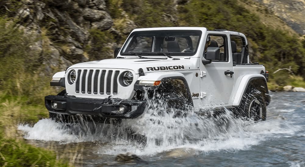A white 2022 Jeep Wrangler Rubicon is shown driving through a river after viewing used Jeeps for sale.