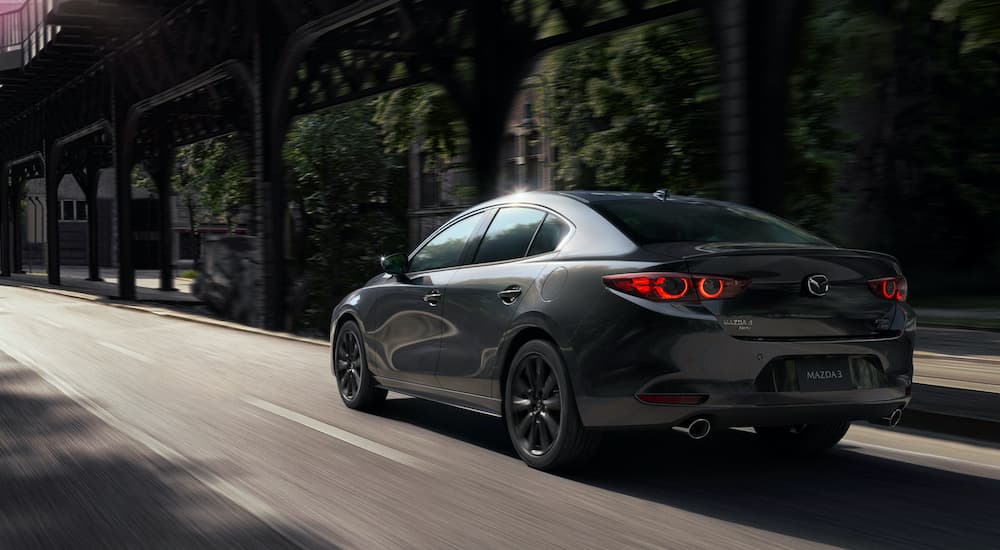 A grey 2021 Mazda3 is shown from the rear driving on a city street after visiting a used Mazda dealership.
