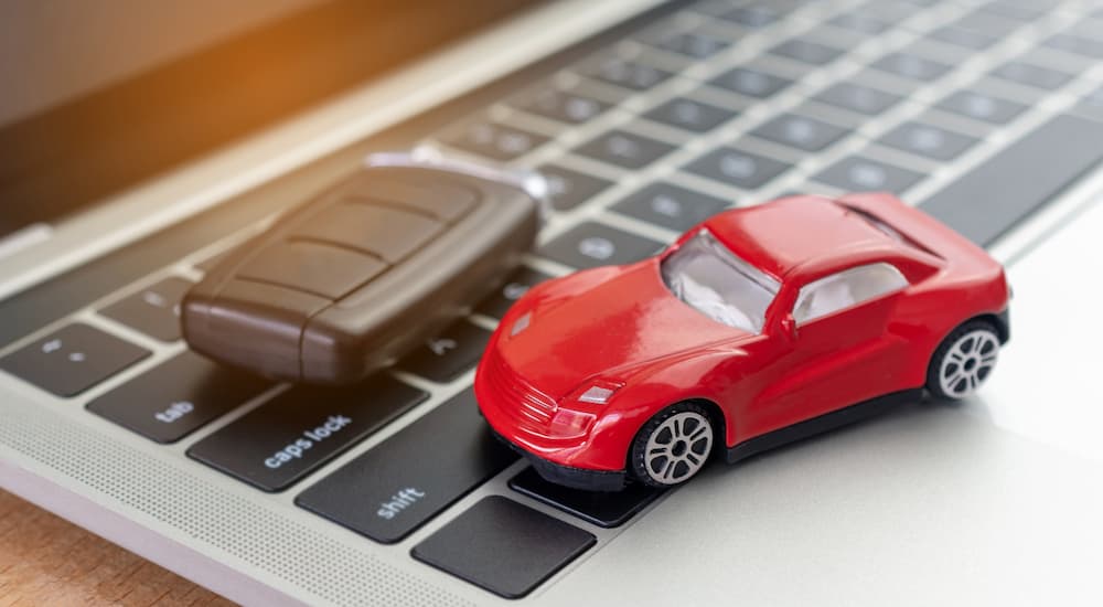 A red toy car is shown on a laptop keyboard.
