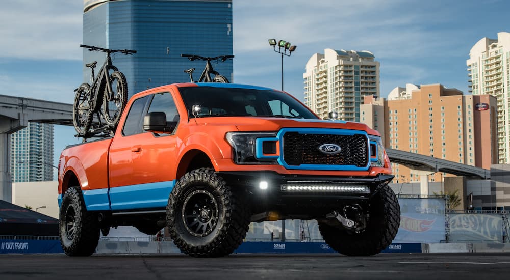 An orange and teal 2018 Ford F-150 is shown parked in front of a city.