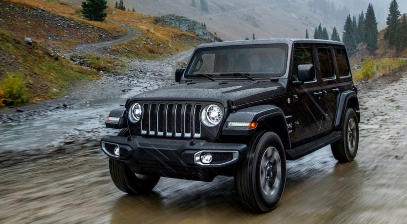 A black 2022 Jeep Wrangler Unlimited is shown from the front at an angle on a mud path after the owner searched for 'Jeep service center'.