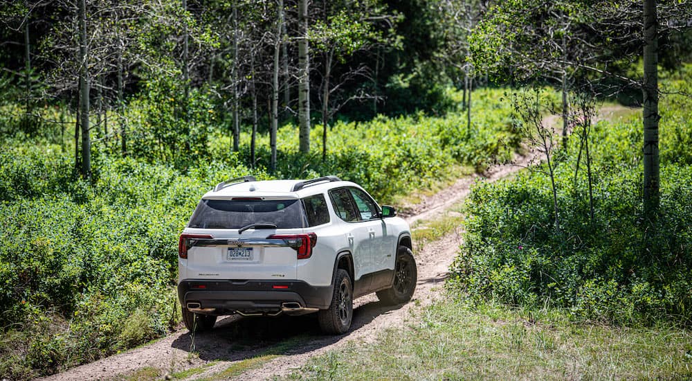 A white 2023 GMC Acadia is shown from the rear on a trail.