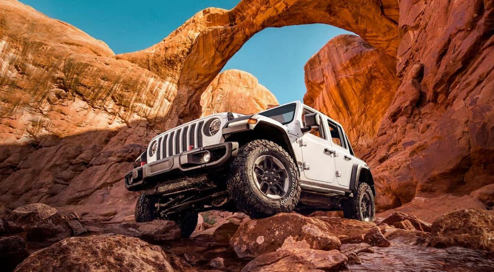 A white 2022 Jeep Wrangler is shown from the front at a low angle in a red rock area.