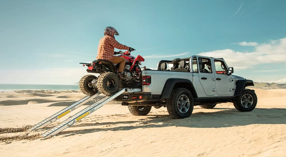 A silver 2022 Jeep Gladiator is shown from the rear while being loaded with an ATV.