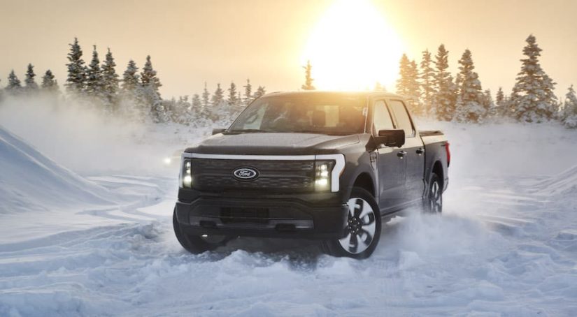 A black 2022 Ford F-150 Lightning is shown from the front at an angle while driving through snow.