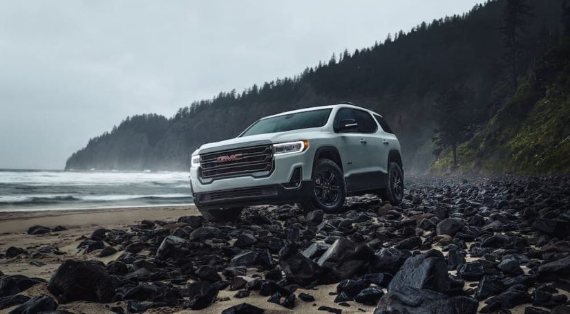 A white 2023 GMC Acadia AT4 is shown from the front at an angle on a rocky beach.