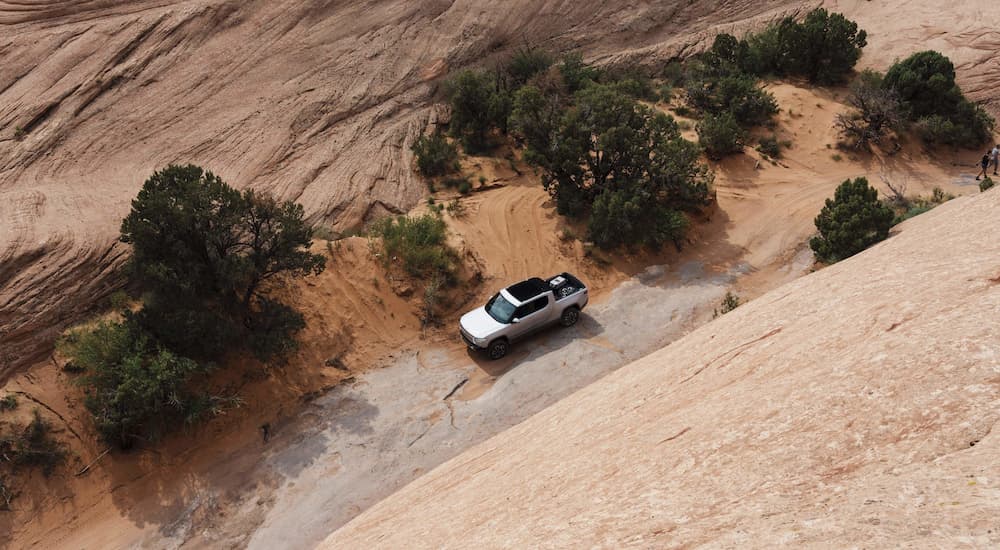 A white 2022 Rivian R1T is shown driving on a dusty trail.