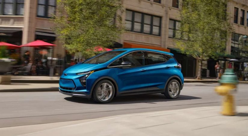 A blue 2023 Chevy Bolt EV is shown from the side driving on a city street.