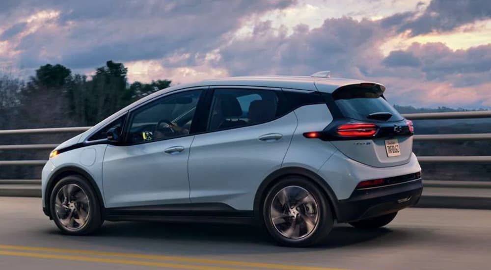 A white 2023 Chevy Bolt EV is shown from the side driving on a bridge.
