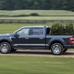 A dark blue 2022 Ford F-150 Powerboost hybrid is shown from the side while hauling trees.