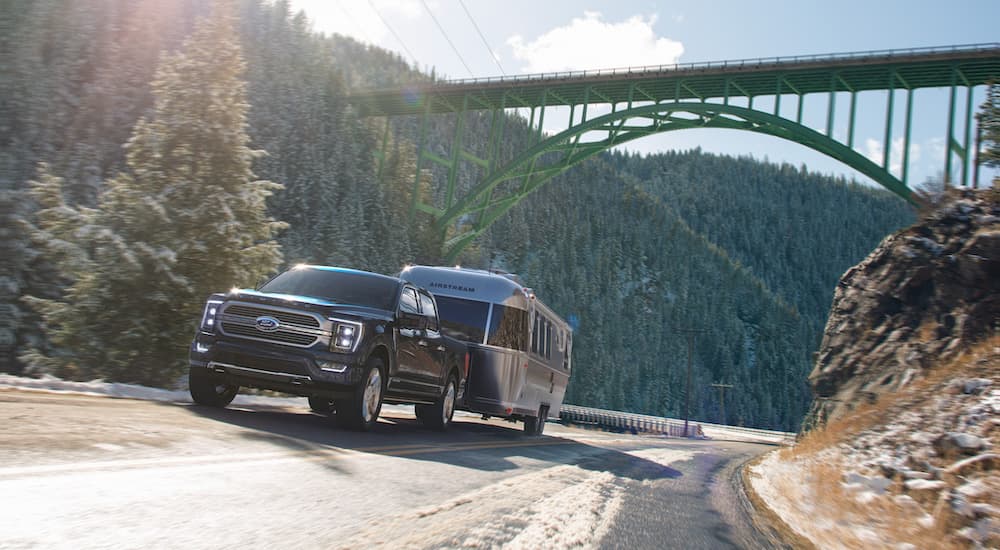 A dark blue 2022 Ford F-150 Powerboost hybrid is shown from the front at an angle while towing a camper.