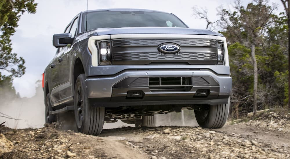 A silver 2022 Ford F-150 Lightning is shown from the front at a low angle while it drives over a dirt hil.
