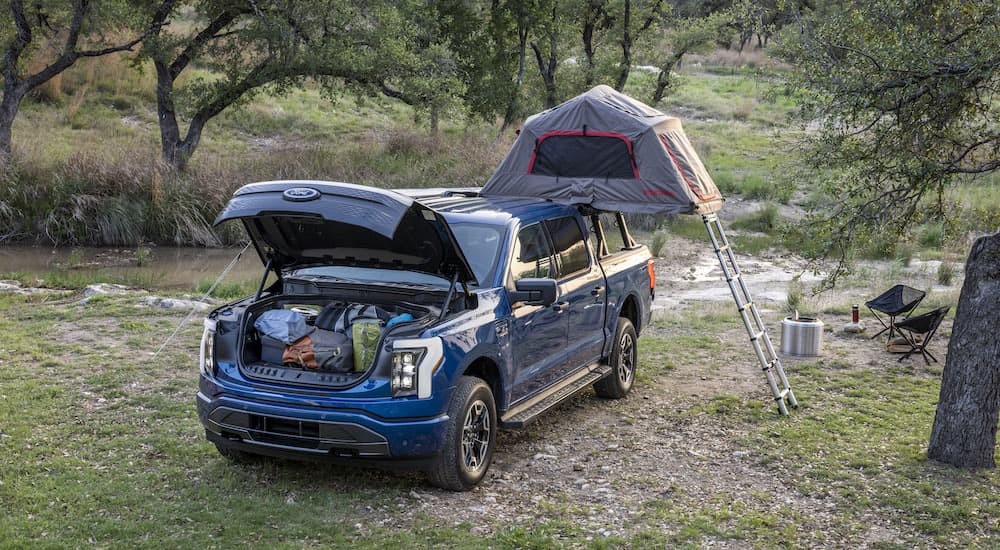 A blue 2022 Ford F-150 Lightning is shown from the front while set up for camping.