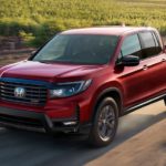 A red 2022 Honda Ridgeline Sport is shown driving on a dirt road after leaving a Honda dealer.