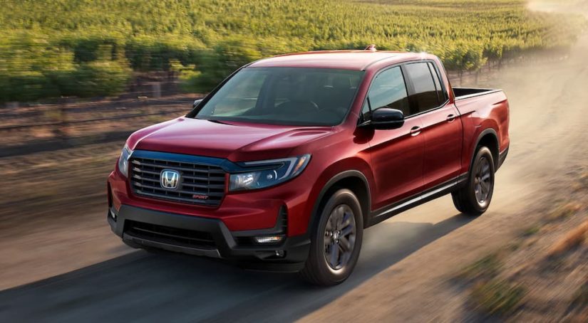 A red 2022 Honda Ridgeline Sport is shown driving on a dirt road after leaving a Honda dealer.