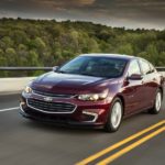 A popular vehicle for online car sales, a purple 2018 Chevy Malibu Hybrid, is shown driving past trees.