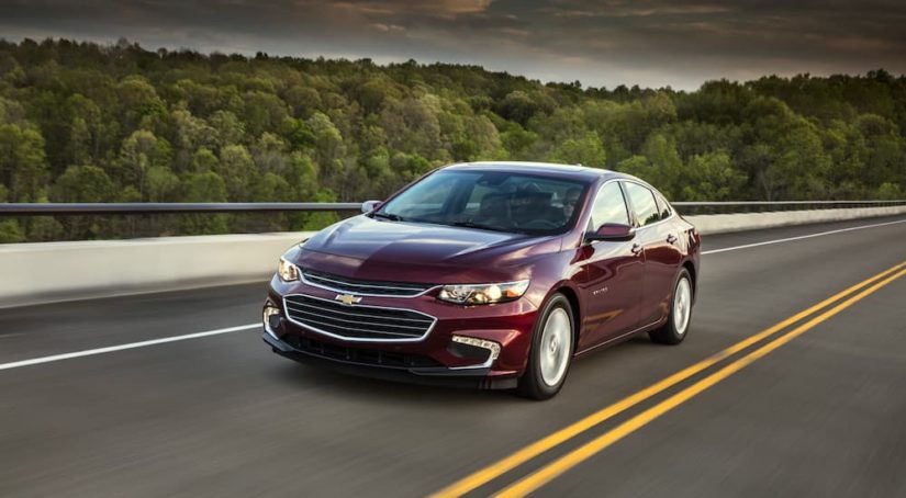 A popular vehicle for online car sales, a purple 2018 Chevy Malibu Hybrid, is shown driving past trees.
