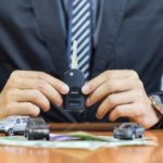 A salesman is shown holding a car key at a car dealership.