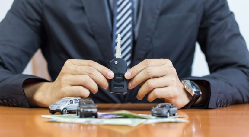 A salesman is shown holding a car key at a car dealership.