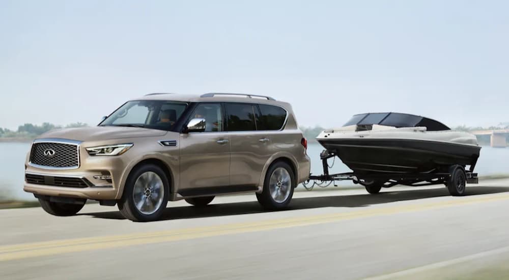 A tan 2022 INFINITI QX80 is shown from the side while towing a boat.