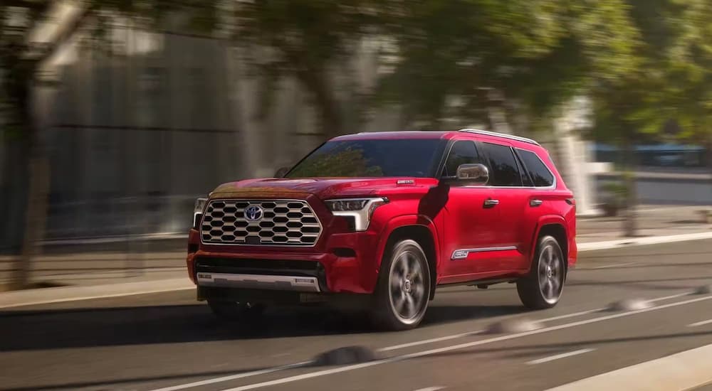 A red 2023 Toyota Sequoia is shwon from the front at an angle on a city street during a 2022 Nissan Armada vs 2022 Toyota Sequoia comparison.