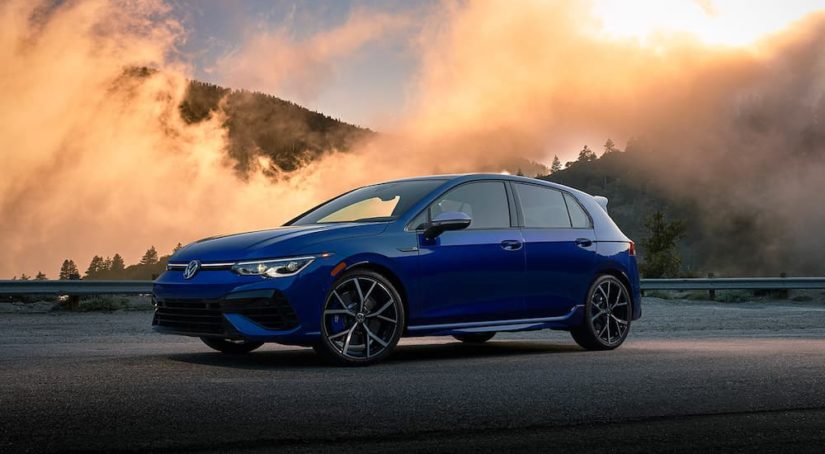 A blue 2022 Volkswagen Golf R is shown from the front at an angle while parked on a forest road.