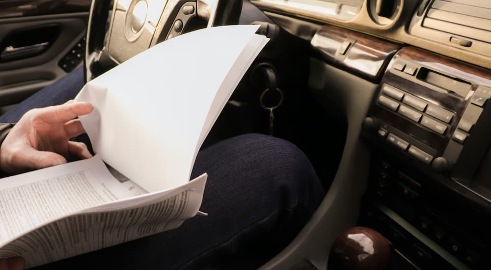 A person is shown looking at paperwork in the front seat of a car.