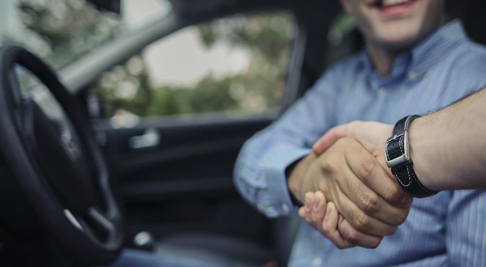 A person is shown shaking hands with a car salesperson.