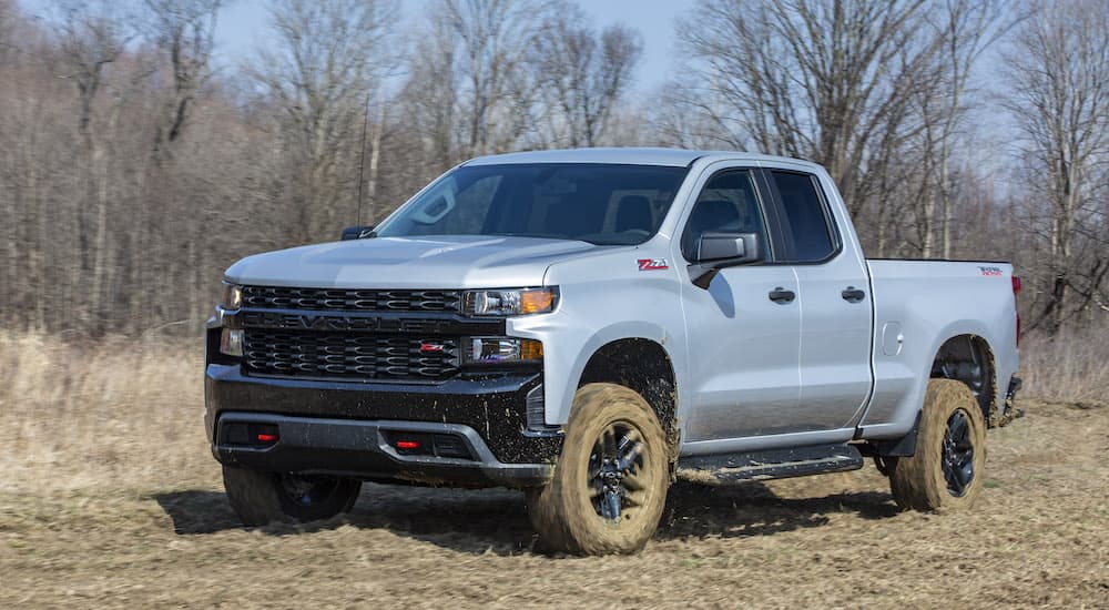 A silver 2022 Chevy Silverado 1500 Custom Trail Boss is shown from the front at an angle while parked off-road.