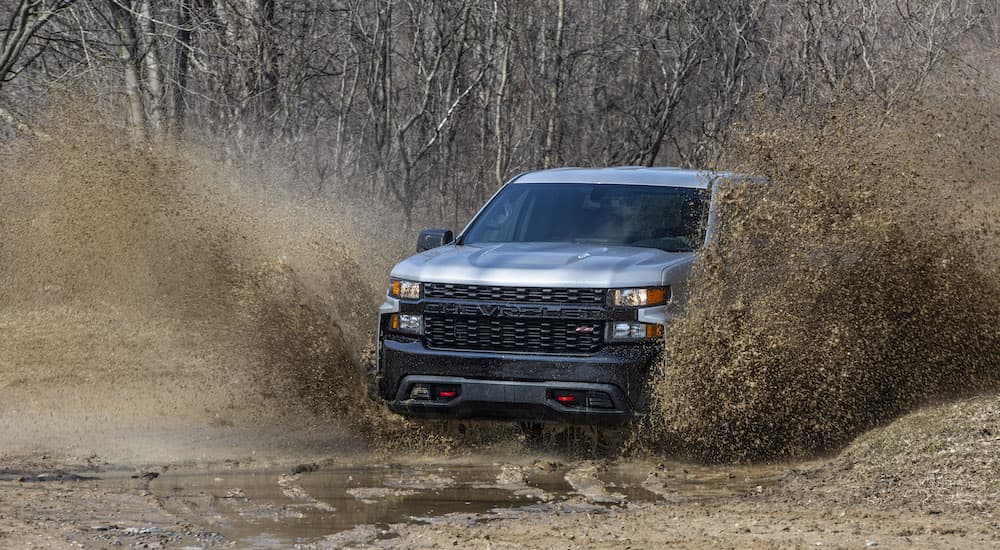 A grey 2020 Chevy Silverado 1500 Custom Trail Boss is shown from the front while driving through mud.