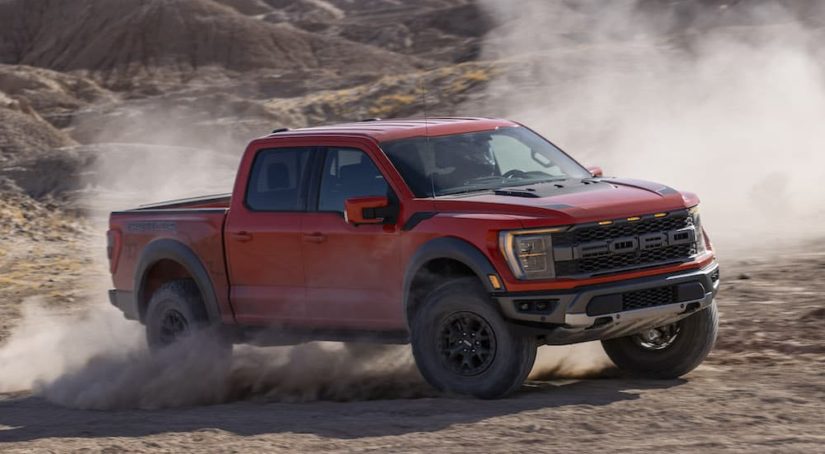 An orange 2021 Ford F-150 Raptor is shown from the side at an angle while sliding off-road.