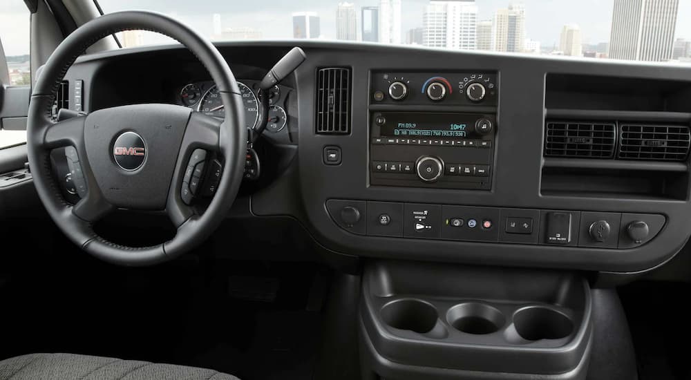 The black interior of a 2022 GMC Savana Cargo Van shows the steering wheel and infotainment screen.