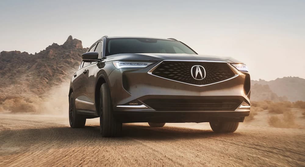 A grey 2023 Acura MDX is shown kicking up dust in the desert.