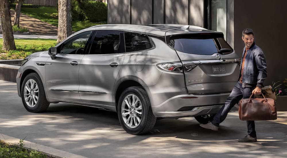 A silver 2023 Buick Enclave is shown from the side parked in front of a house.