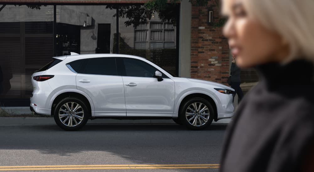 A white 2023 Mazda CX-5 is shown from the side parked on a city street.