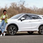A woman is shown leaning up against the hood of a white 2022 Mitsubishi Eclipse Cross.