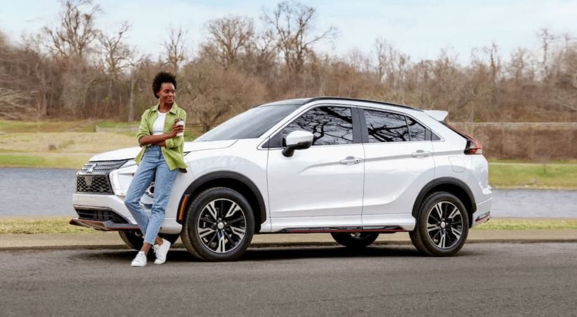 A woman is shown leaning up against the hood of a white 2022 Mitsubishi Eclipse Cross.