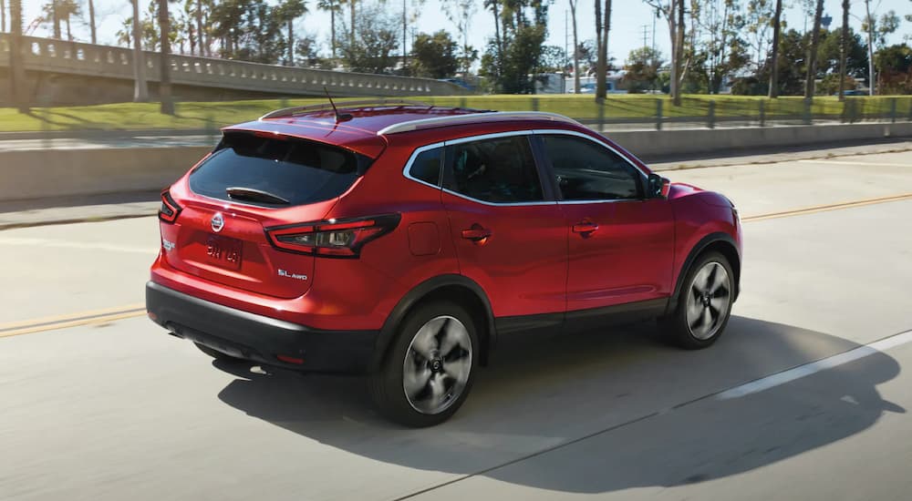 A red 2022 Nissan Rogue is shown from a rear angle driving on an open road.