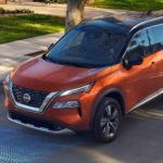 An orange 2022 Nissan Rogue is shown driving on a street near a Nissan Rogue dealer.