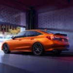 An orange 2022 Honda Civic Si is shown from the rear at an angle while parked in an urban area.