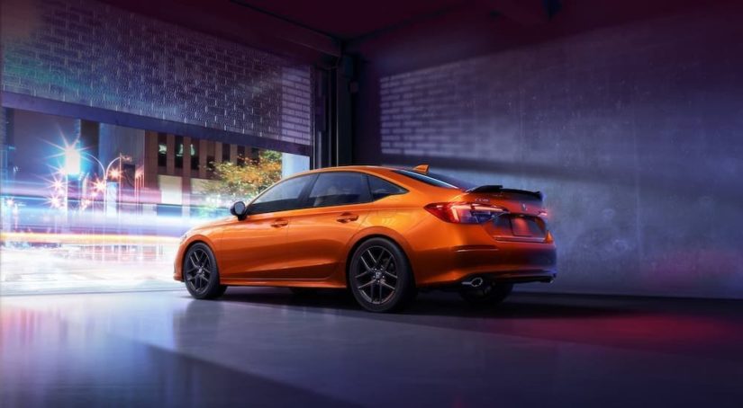 An orange 2022 Honda Civic Si is shown from the rear at an angle while parked in an urban area.
