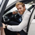A man is shown opening the door of a white car.