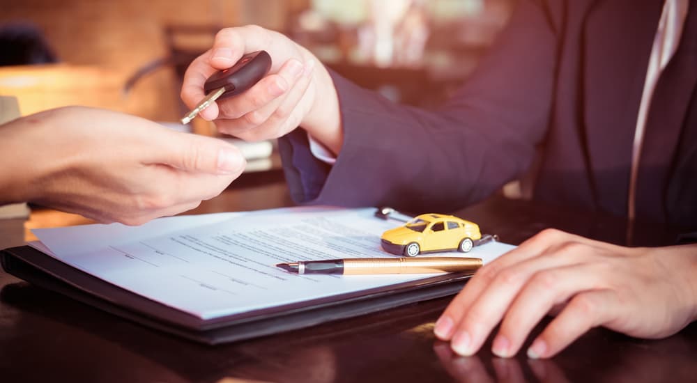 Two people are shown exchanging a car key over paperwork.