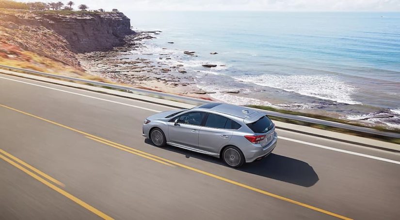 A silver 2022 Subaru Impreza is shown driving on a coastal road.