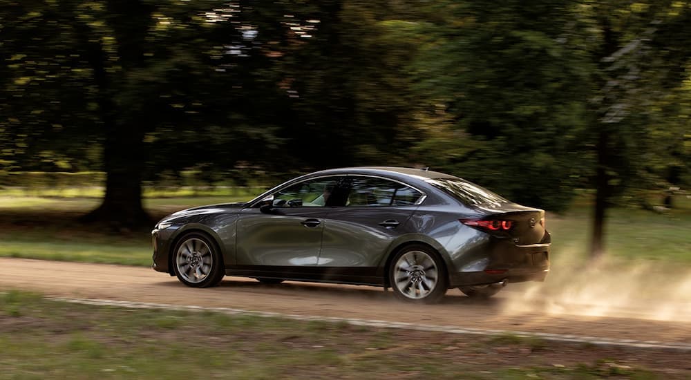 A car with a high trade-in value, a grey 2020 Mazda3 is shown from the side driving on a dirt road.